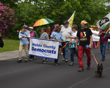 Group of WCDC members walking in the Pride Parade with the Waldo County Dems blue and white banner.