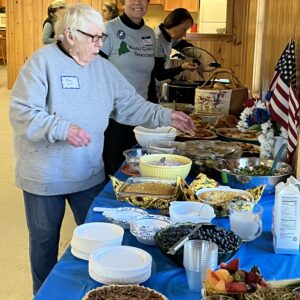 Mary Lou, and Karen put the finishing touches on a long table loaded with food for the potluck and decorated with blue tablecloths, flowers, and American flags.