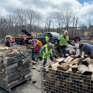 Loaded quarter-cord baskets in foreground with safety-vested volunteers using splitters in background