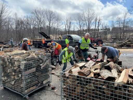Loaded quarter-cord baskets in foreground with safety-vested volunteers using splitters in background