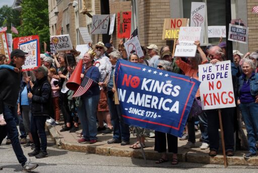 Protesters on a street corner with "No Kings" signs.