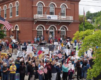 View of Belfast Post Office Square with protesters filling the parking lot with signs and US flags.