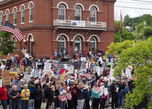 View of Belfast Post Office Square with protesters filling the parking lot with signs and US flags.