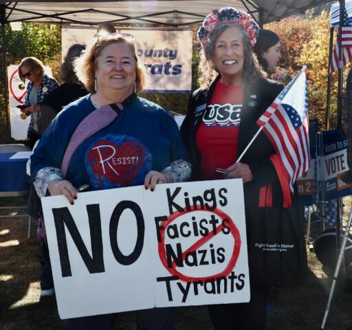 Rep. Jan Dodge, wearing a red tee and holding a US flag, is standing with a protester at the Oct. 18 No Kings Rally. The protester is wearing a blue tee that says RESIST and holding a sign that says No Kings Fascists Nazis Tyrants