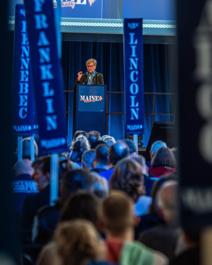 U.S. Representative Chellie Pingree speaks in front of the audience and county signs.