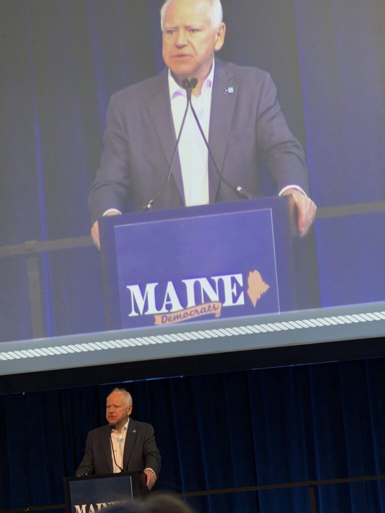 Minnesota Governor Tim Walz speaks at the convention below his image on the big screen.
