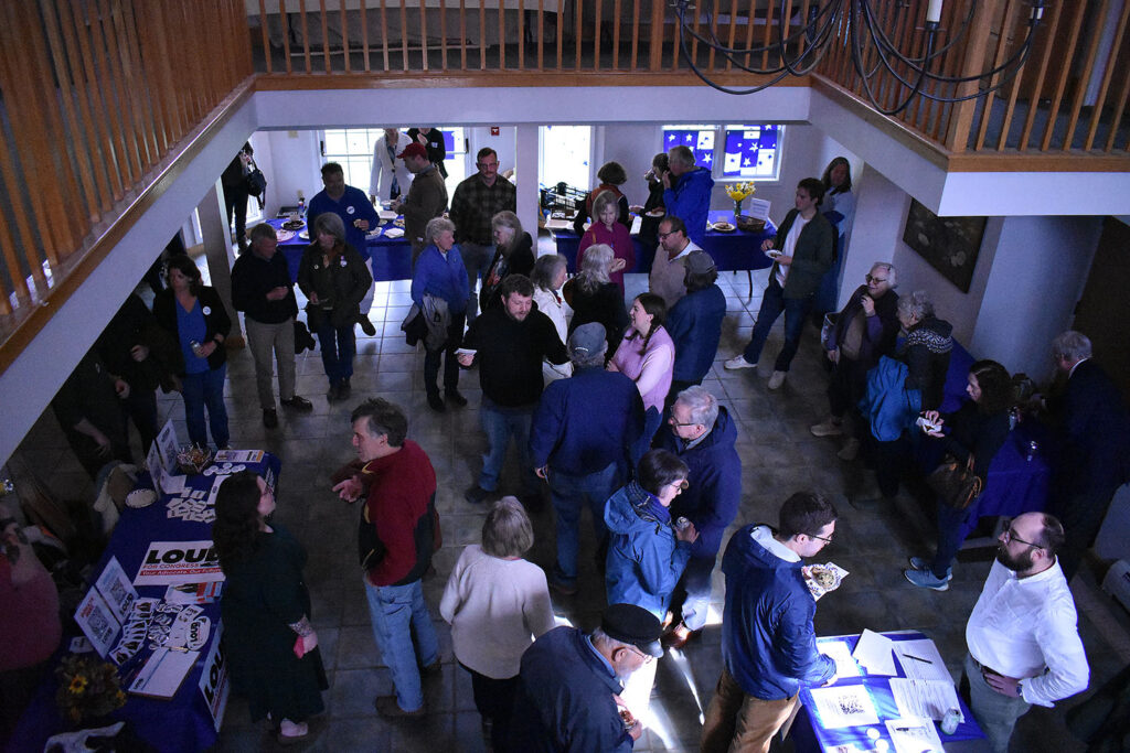 A view of the reception area, where dozens of people are chatting in small groups, looking down from a balcony. There are campaign materials on tables around the outside of the room.