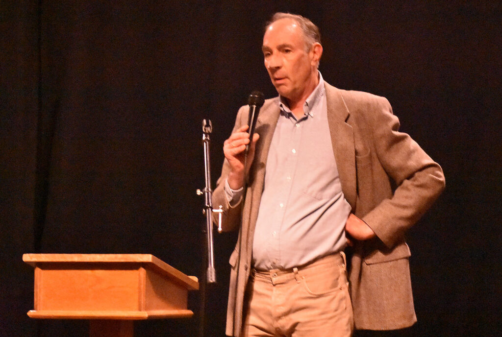 Moderator Tom Groening speaks into a microphone on the forum stage.