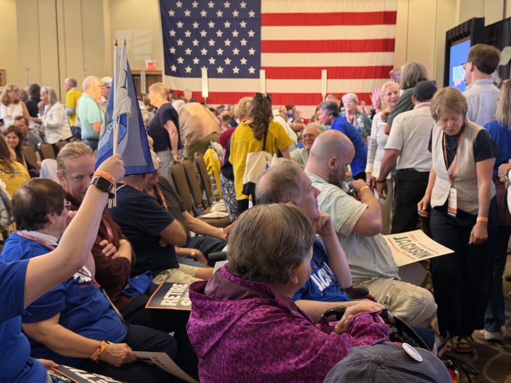 Delegates mingle on the convention floor in front of a huge American flag.